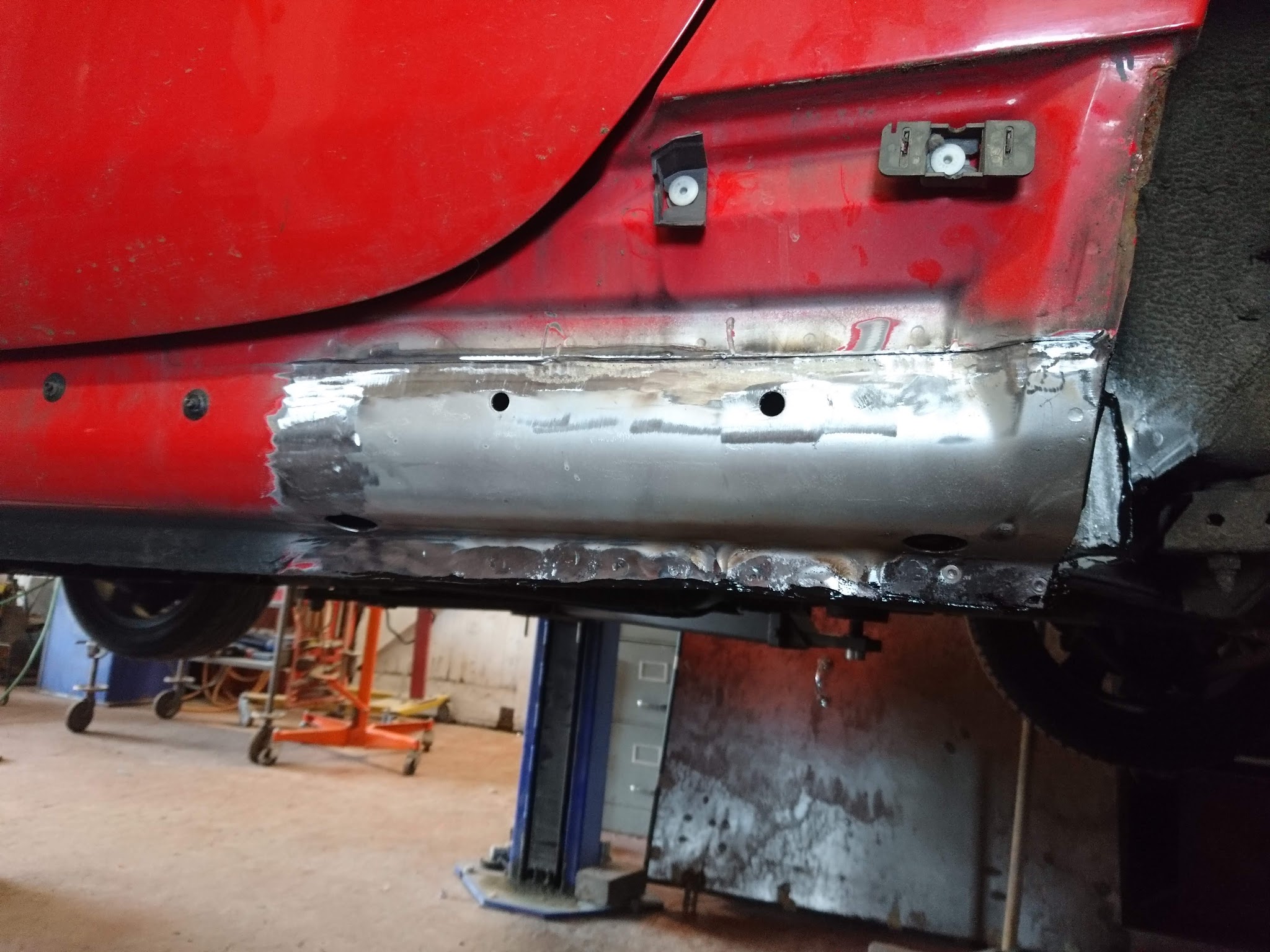 Panel and sill repair under way on a red car on the ramp